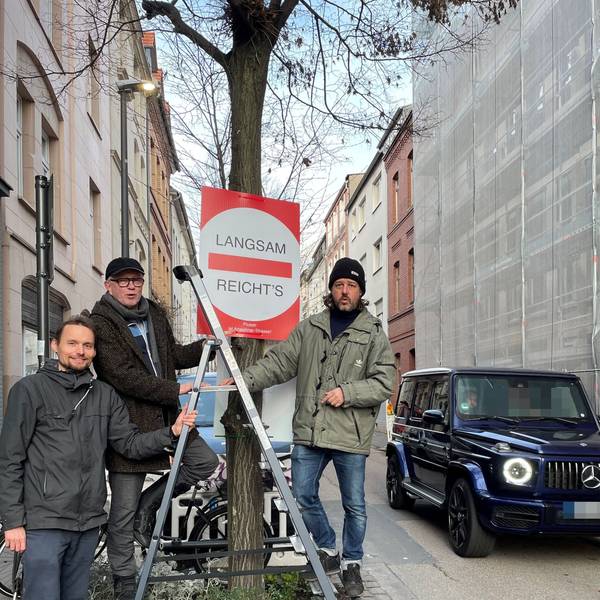 Drei Männer stehen um ein Baumbeet herum. Sie haben ein Schild aufgehängt.