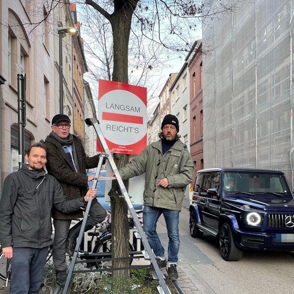 Drei Männer stehen um ein Baumbeet herum. Sie haben ein Schild aufgehängt.