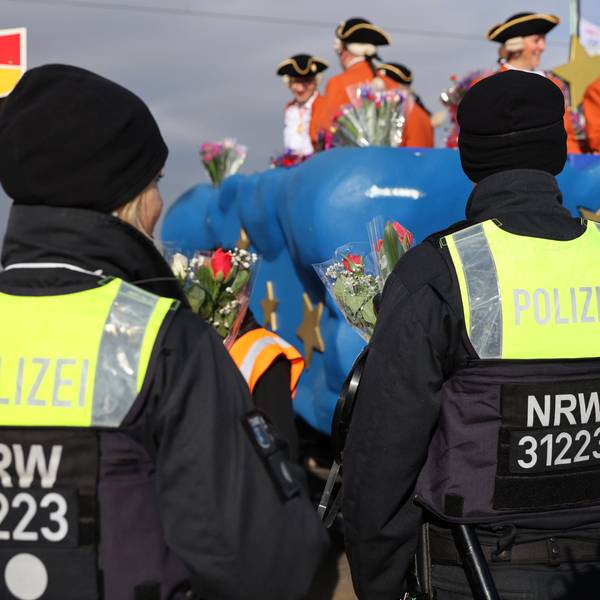 Polizisten stehen am Rand eines Karnevalszuges.