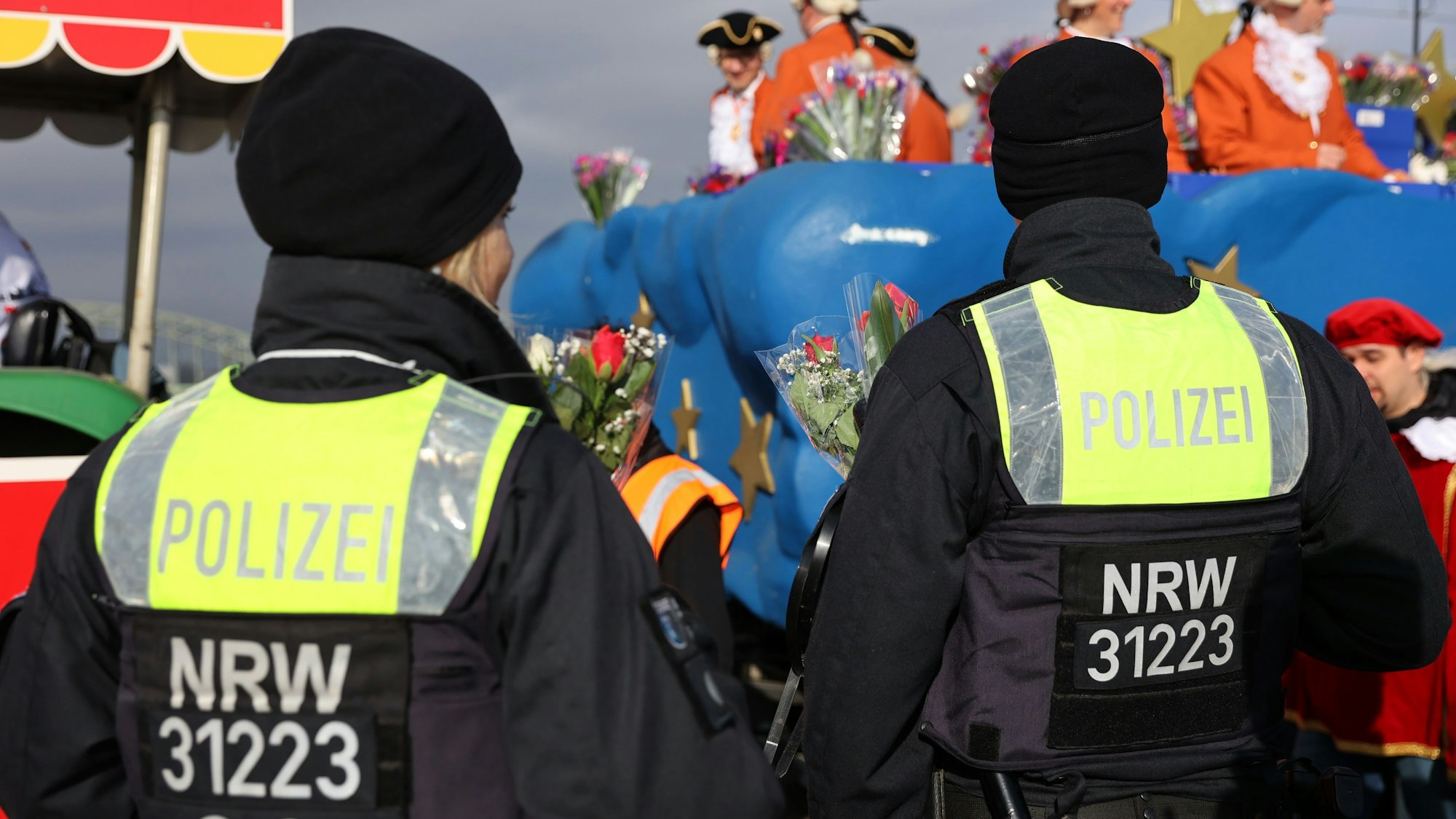 Polizisten stehen am Rand eines Karnevalszuges.
