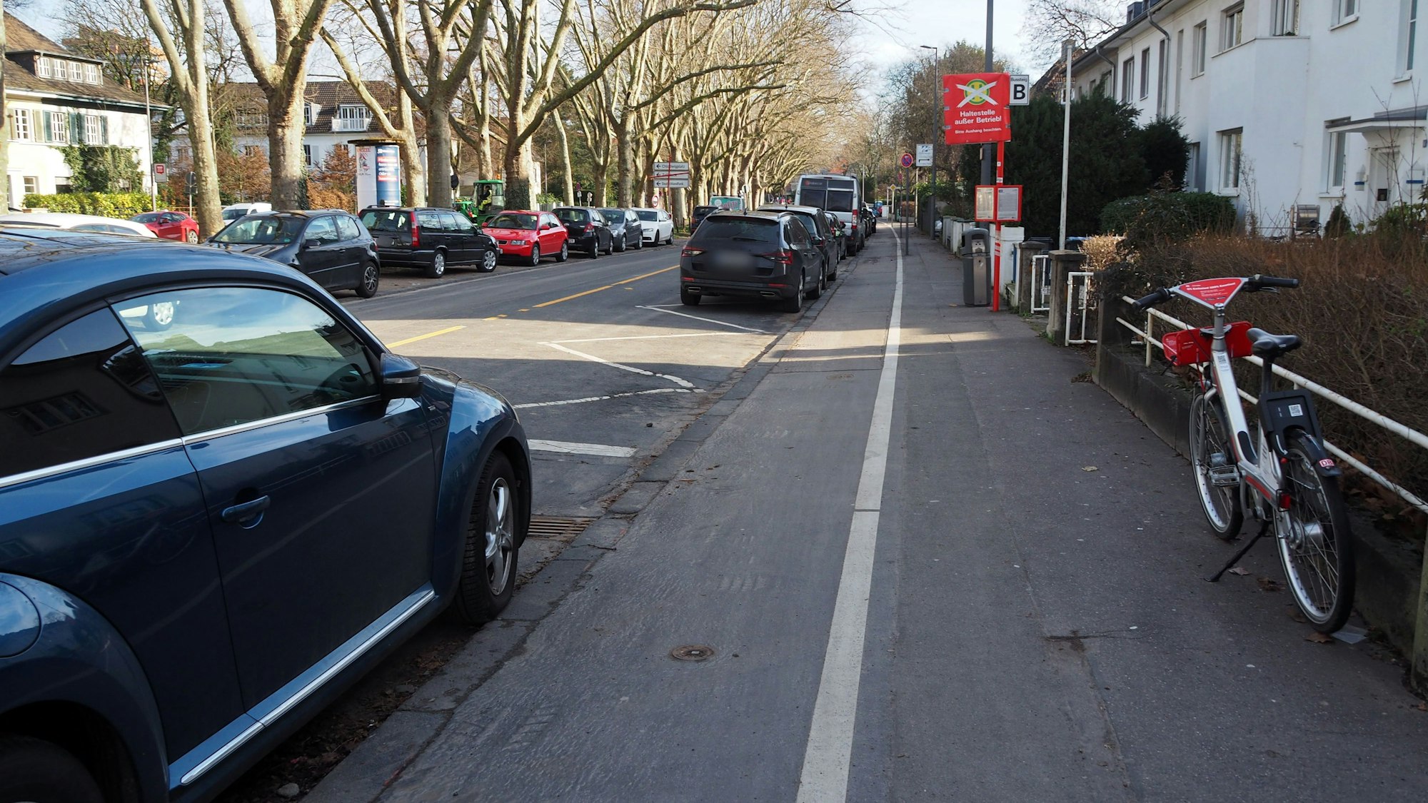 Blick in eine Straße mit parkenden Autos und einem für Radfahrer und Fußgänger aufgeteilten Gehweg.