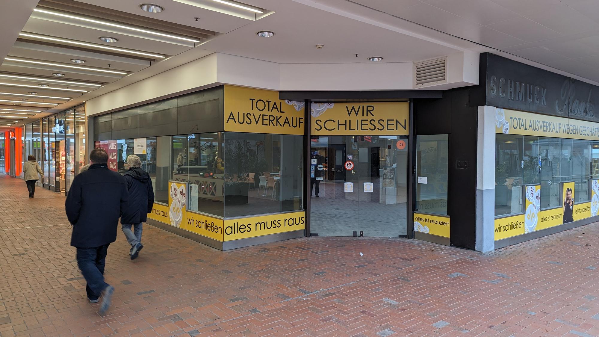 An den Fenstern des leeren Ladenlokals kleben Schilder mit der Aufschrift „Wir schließen“ und „Totalausverkauf“.