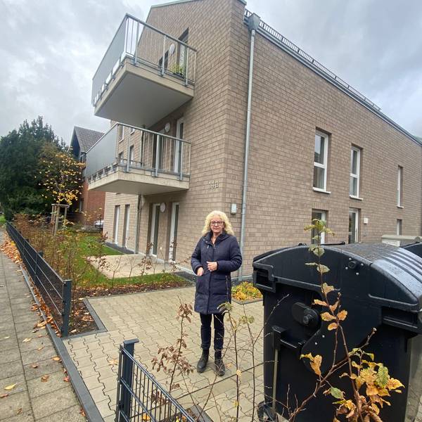 Eine Frau steht auf einer Freifläche, die zu einem Mehrfamilienhaus gehört.