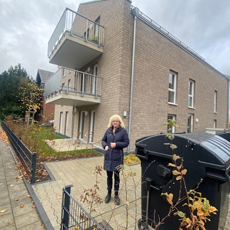 Eine Frau steht auf einer Freifläche, die zu einem Mehrfamilienhaus gehört.