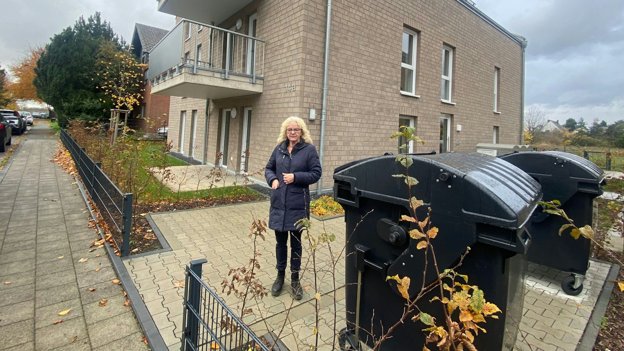 Eine Frau steht auf einer Freifläche, die zu einem Mehrfamilienhaus gehört.