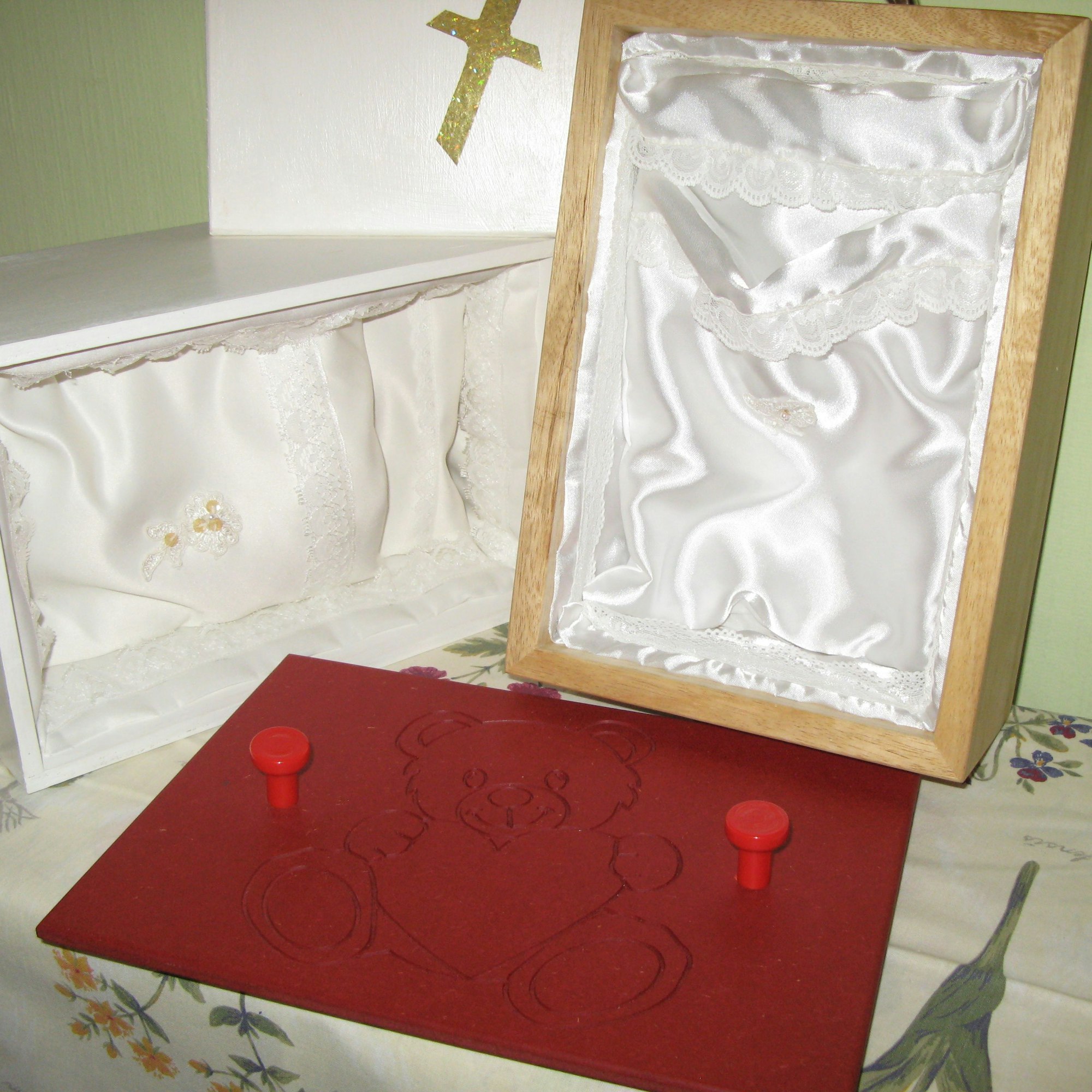 Das Bild zeigt Holzkästen, die mit weißem Seidenstoff ausgekleidet sind und als Särge für totgeborene Kinder dienen.