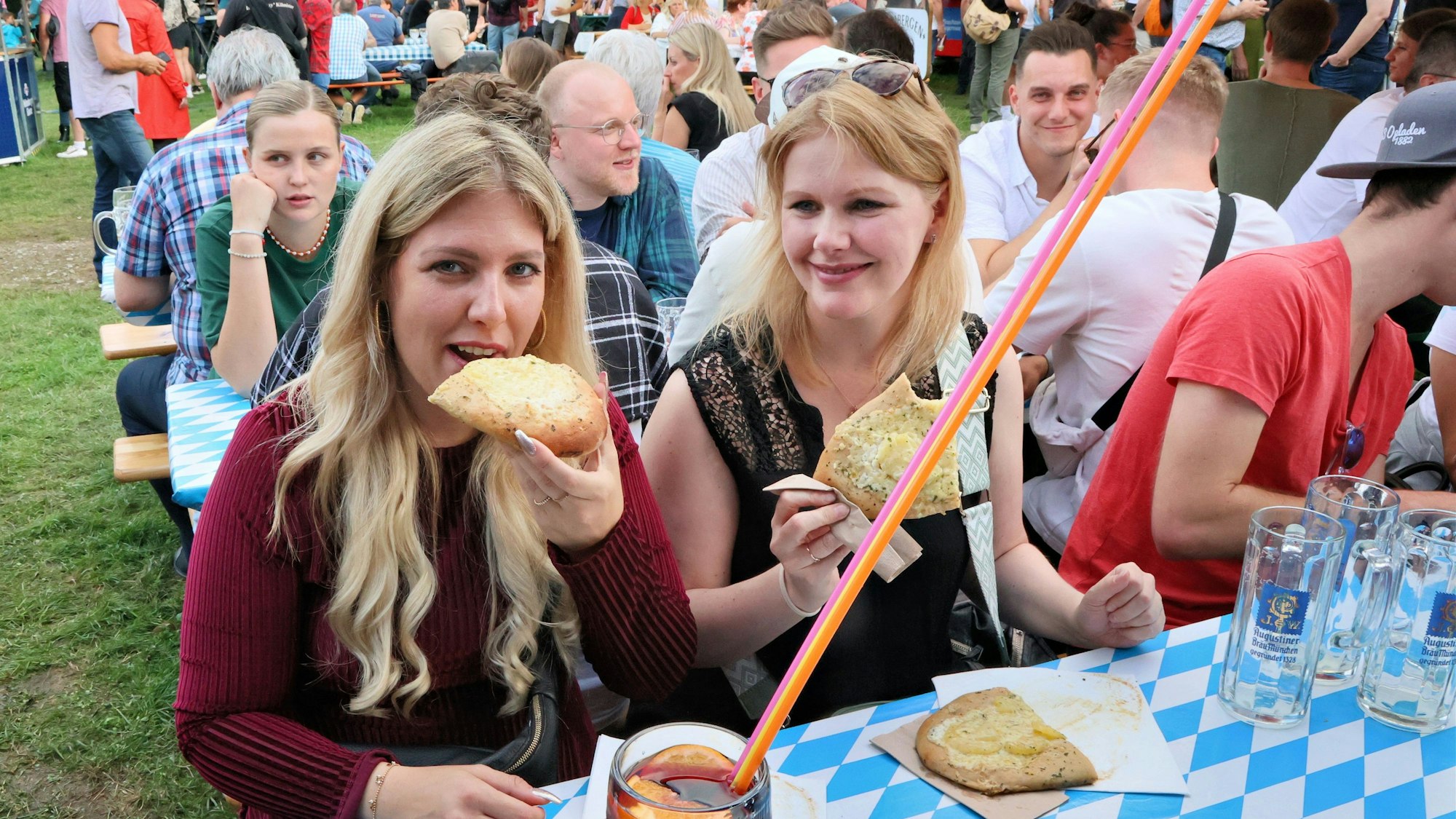 Zwei Besucherinnen sitzen an einer Bierzeltgarnitur und essen und trinken.