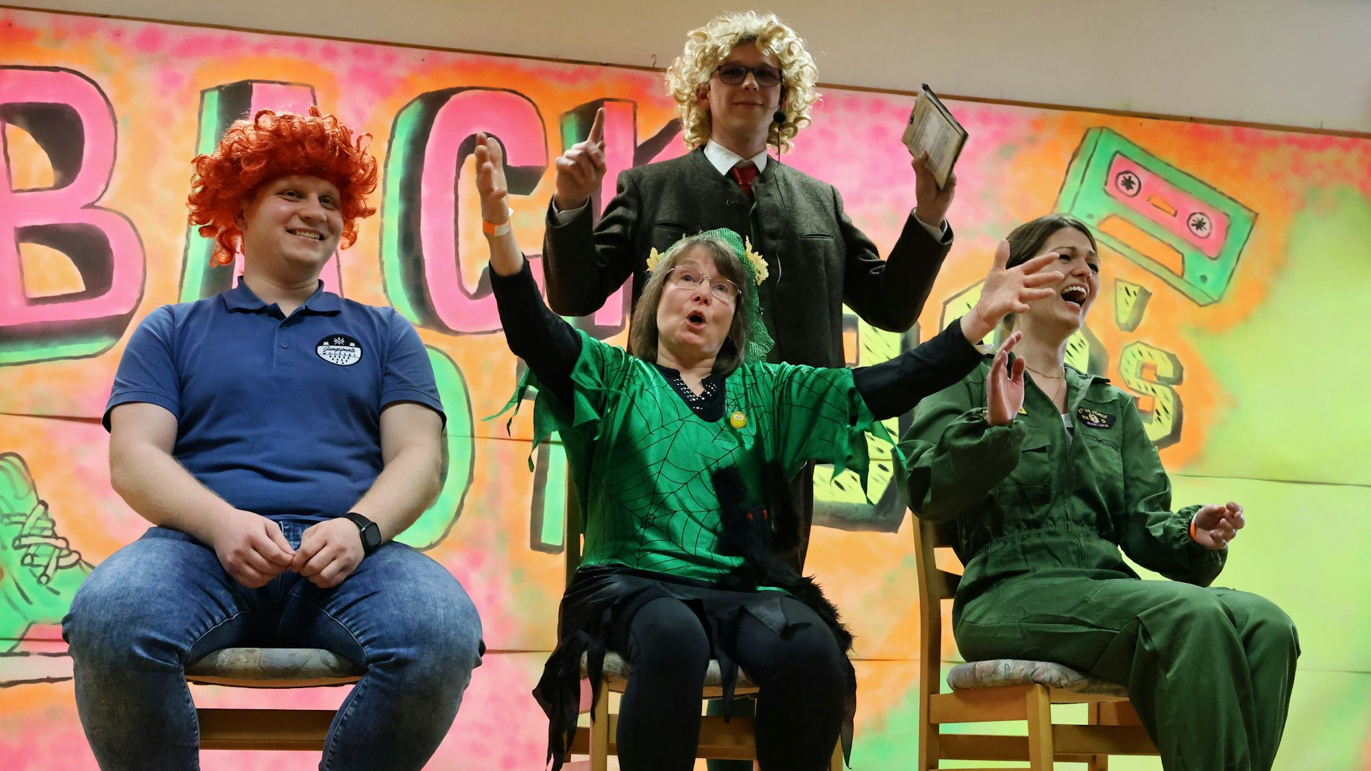 Die drei kostümierten Kandidaten aus dem Publikum sitzen auf Stühlen, dahinter moderiert stehend Markus Klinkhammer.