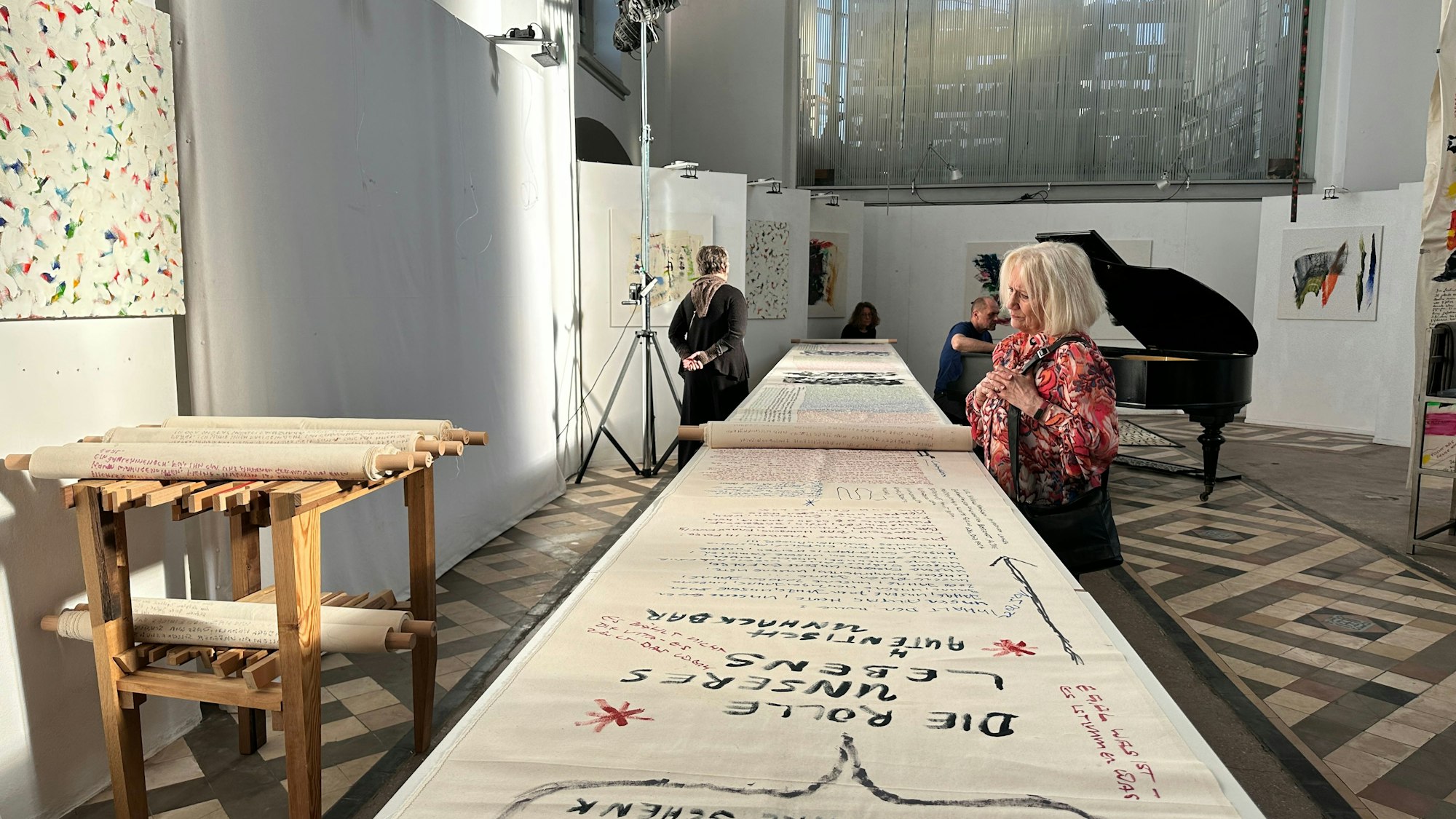 Eine lange Rolle liegt auf einem sehr langen Tisch. Eine Besucherin begutachtet sie.