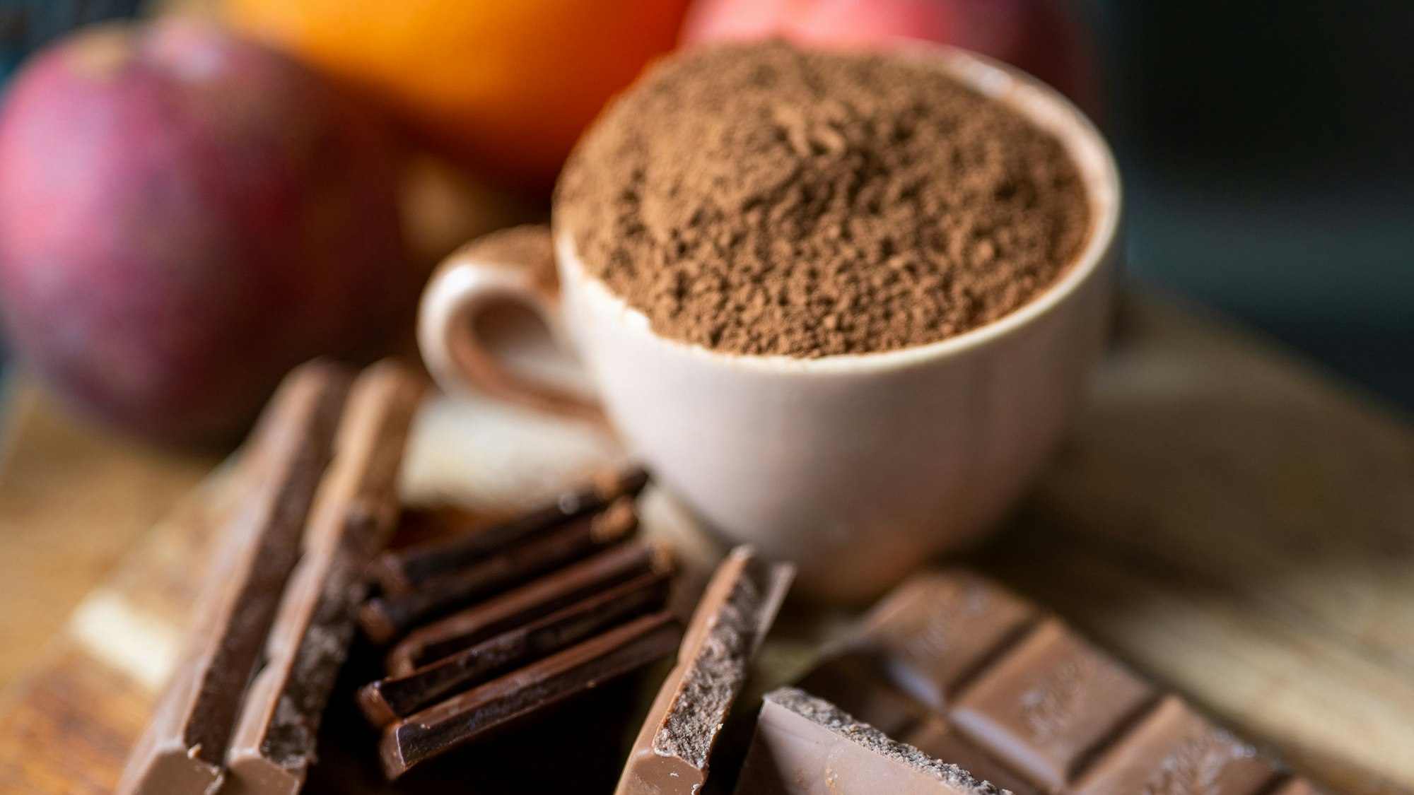 Vollmilchschokolade liegt neben einer mit Kakaopulver gefüllten Tasse auf einem Holzbrett in der Küche.