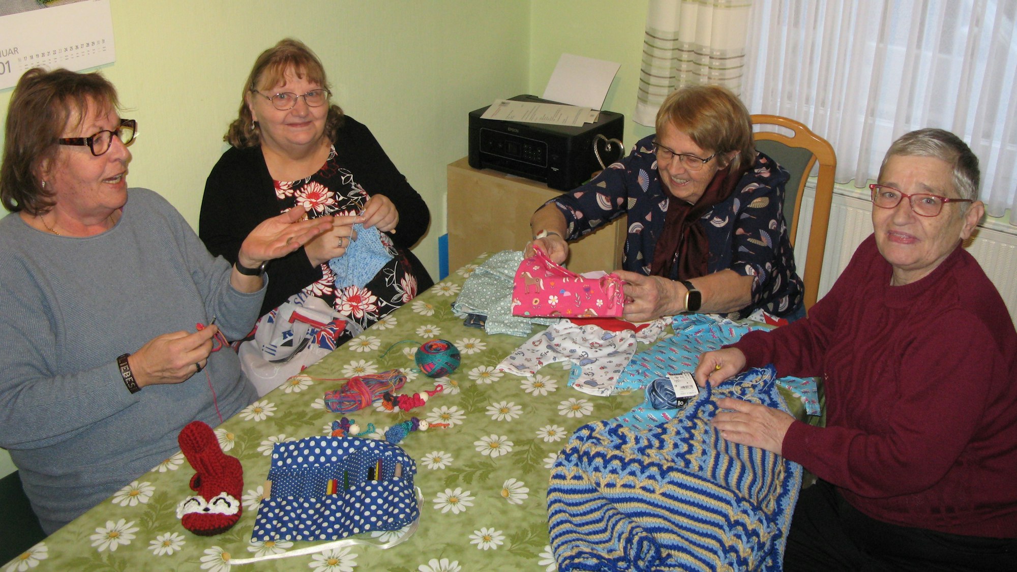 Vier Frauen sitzen mit ihren Handarbeiten an einem Esstisch.