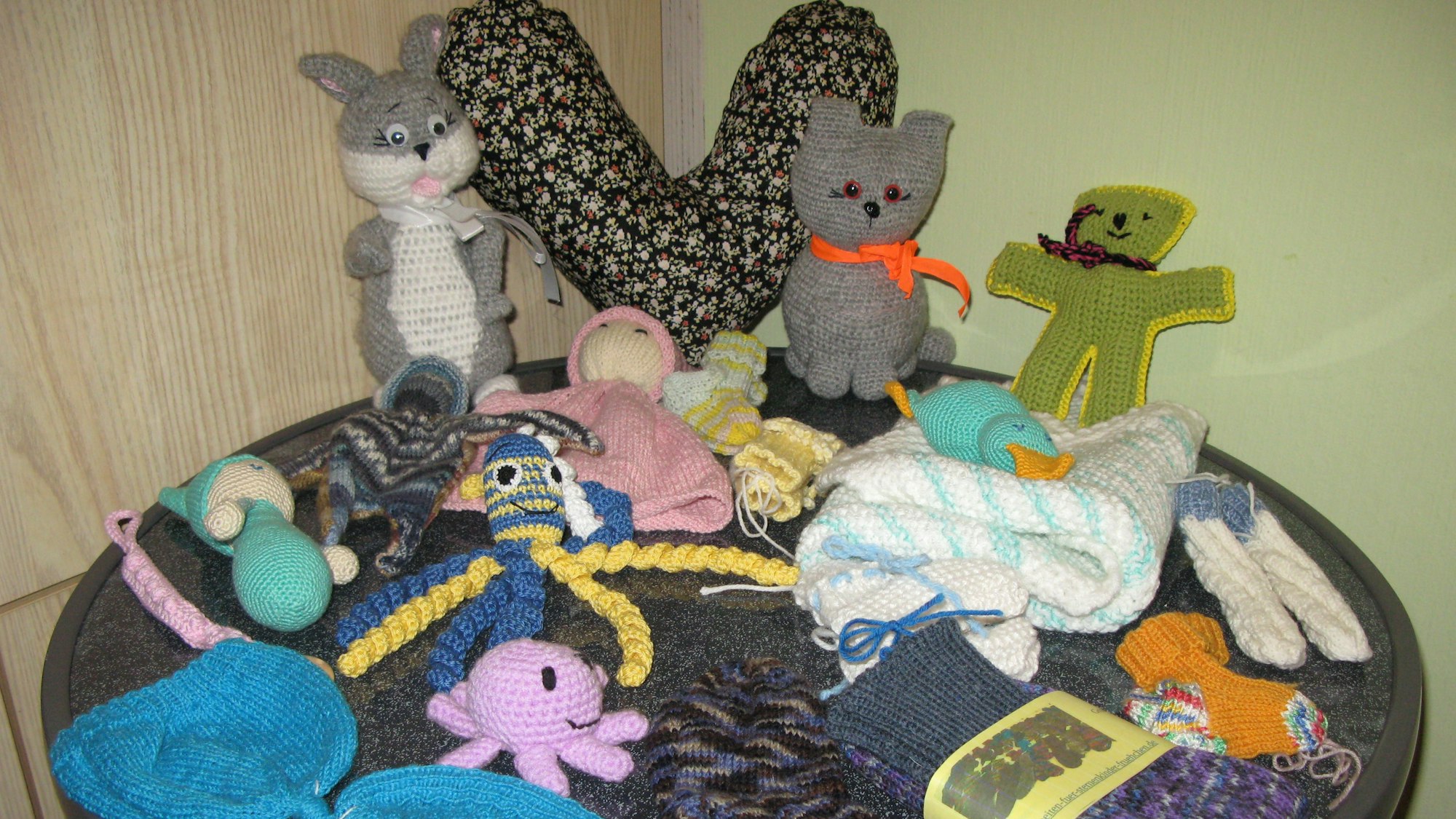Auf einem Tisch liegen kleine gehäkelte Kuscheltiere und Püppchen.