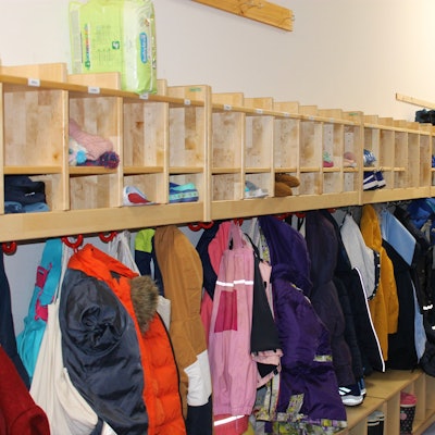 Das Bild zeigt eine Kita-Garderobe, an der viele bunte Jacken hängen.