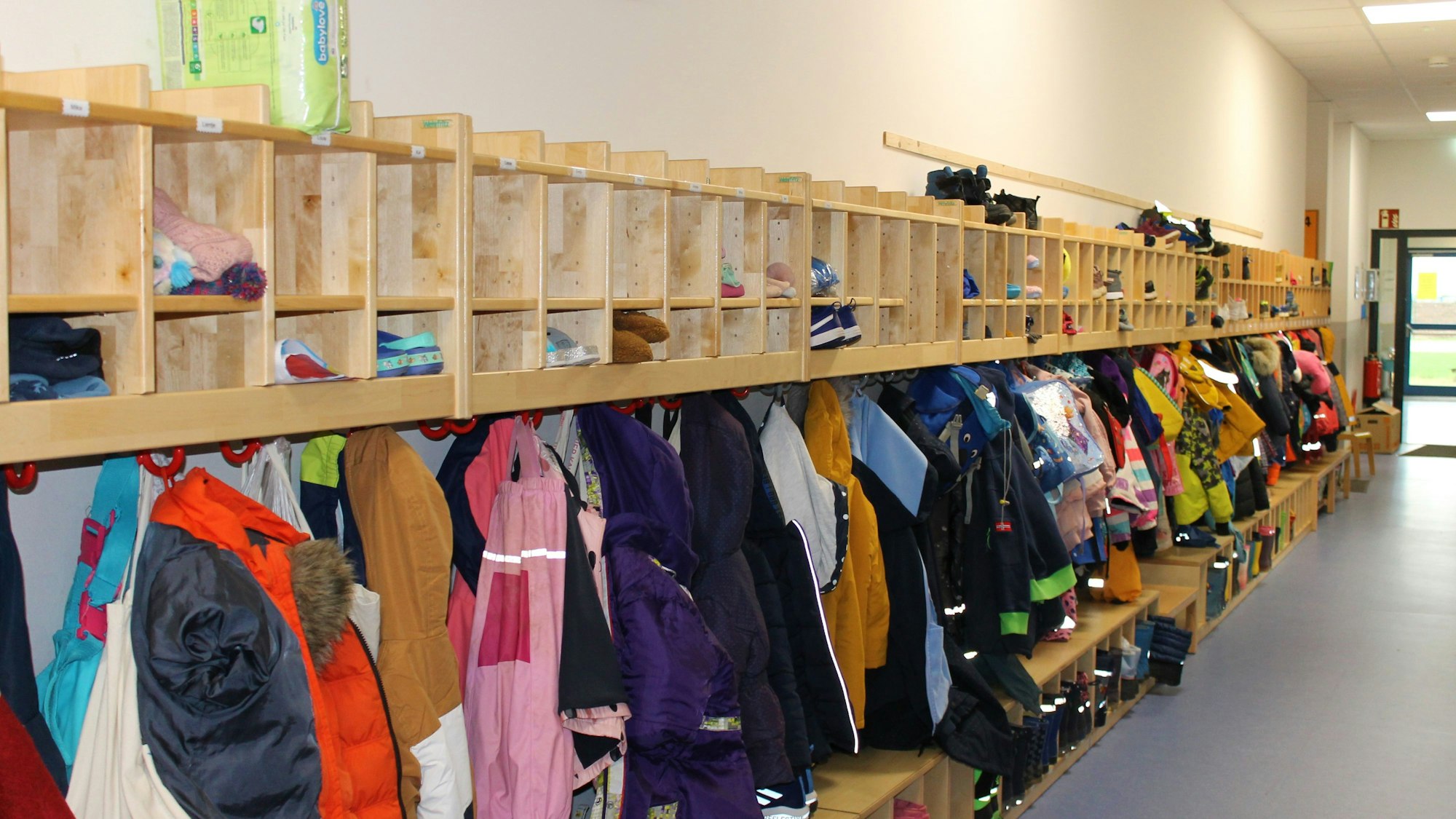 Das Bild zeigt eine Kita-Garderobe, an der viele bunte Jacken hängen.