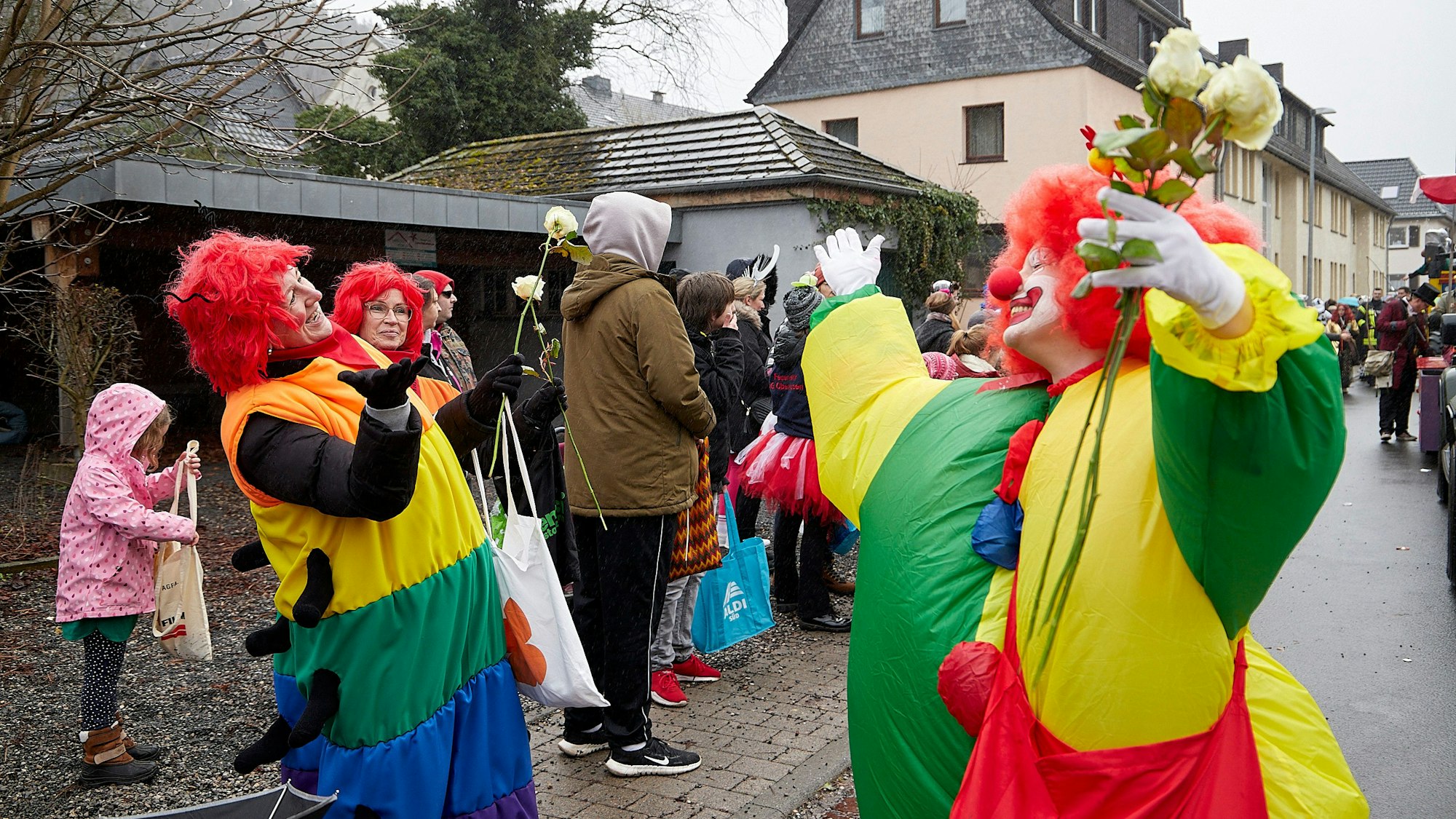 Bei einem Karnevalszug feiern zwei als bunte Clowns verkleidete Jecke in Schleiden.