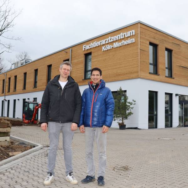 Zwei Männer stehen vor einem neuen zweistöckigen Gebäude mit der Aufschrift Fachtierarztzentrum Köln-Merheim.
