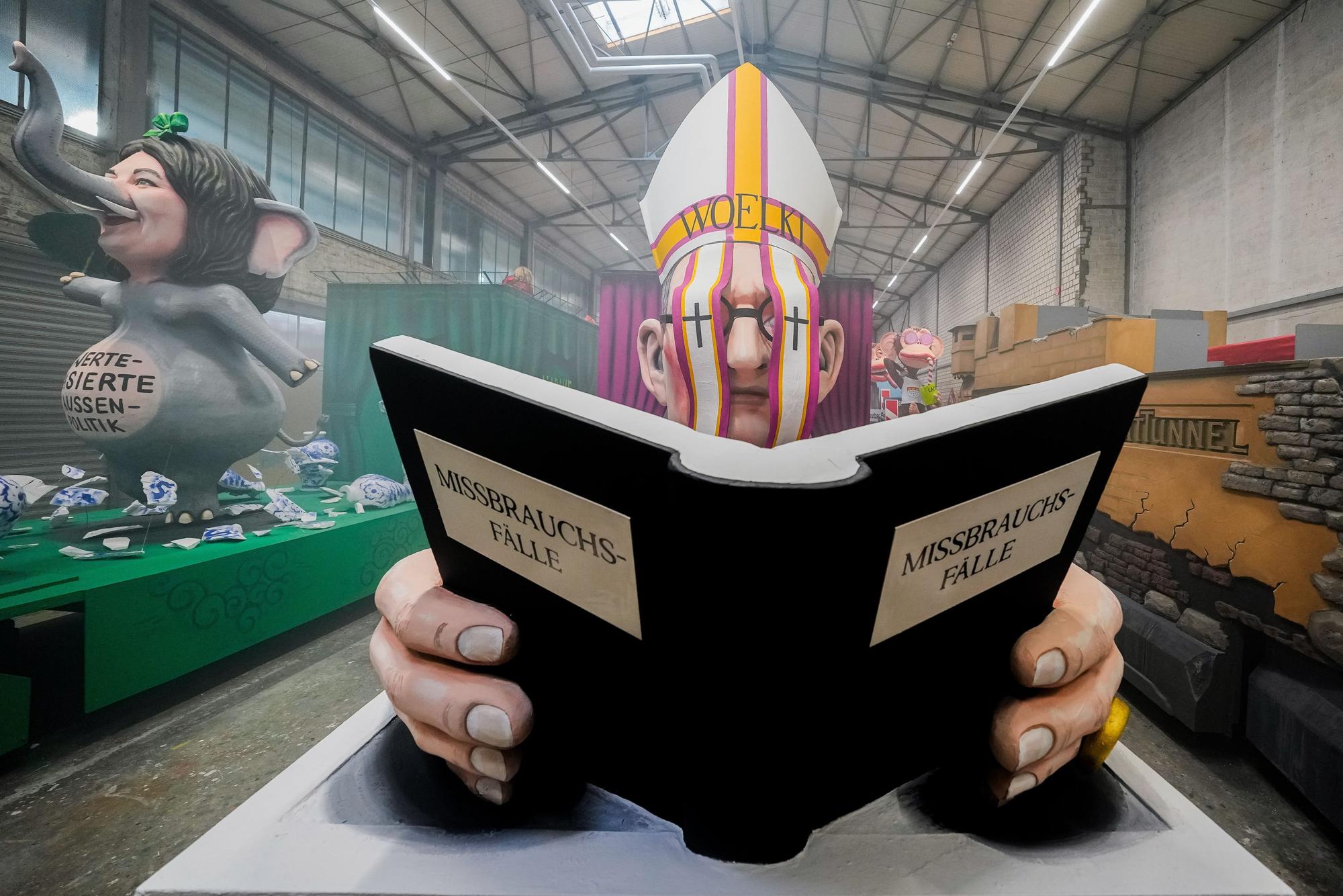 Ein Motivwagen, der Kardinal Woelki mit einem Buch mit der Aufschrift ·Missbrauchsfälle· zeigt, steht beim Richtfest für den Kölner Rosenmontagszug im Karnevalsmuseum.