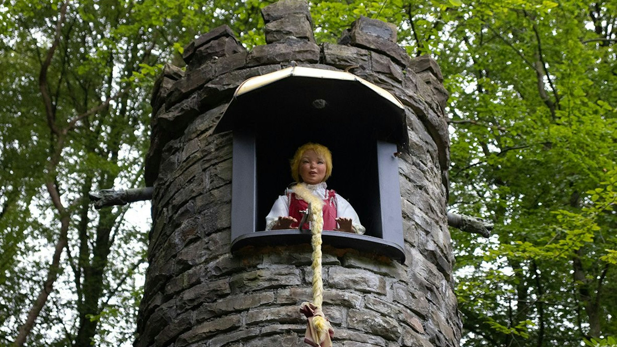 Eine Puppe, die Rapunzel darstellt, schaut aus einem Turm, der das Märchenhaus im Märchenwald in Altenberg darstellt.