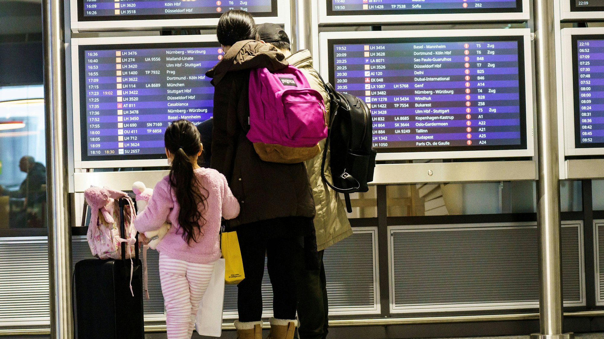 Eine Familie steht an der Anzeigetafel an einem Bahnhof.