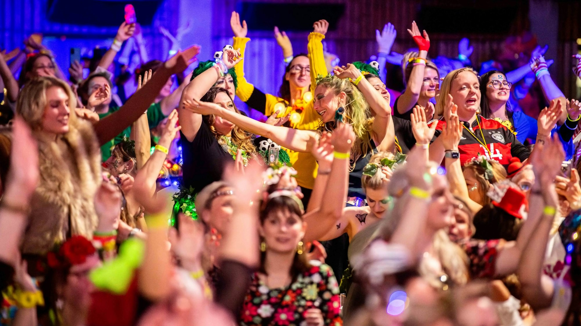 Das Bild zeigt zahlreiche kostümierte Frauen, die die Hände in die Luft strecken.