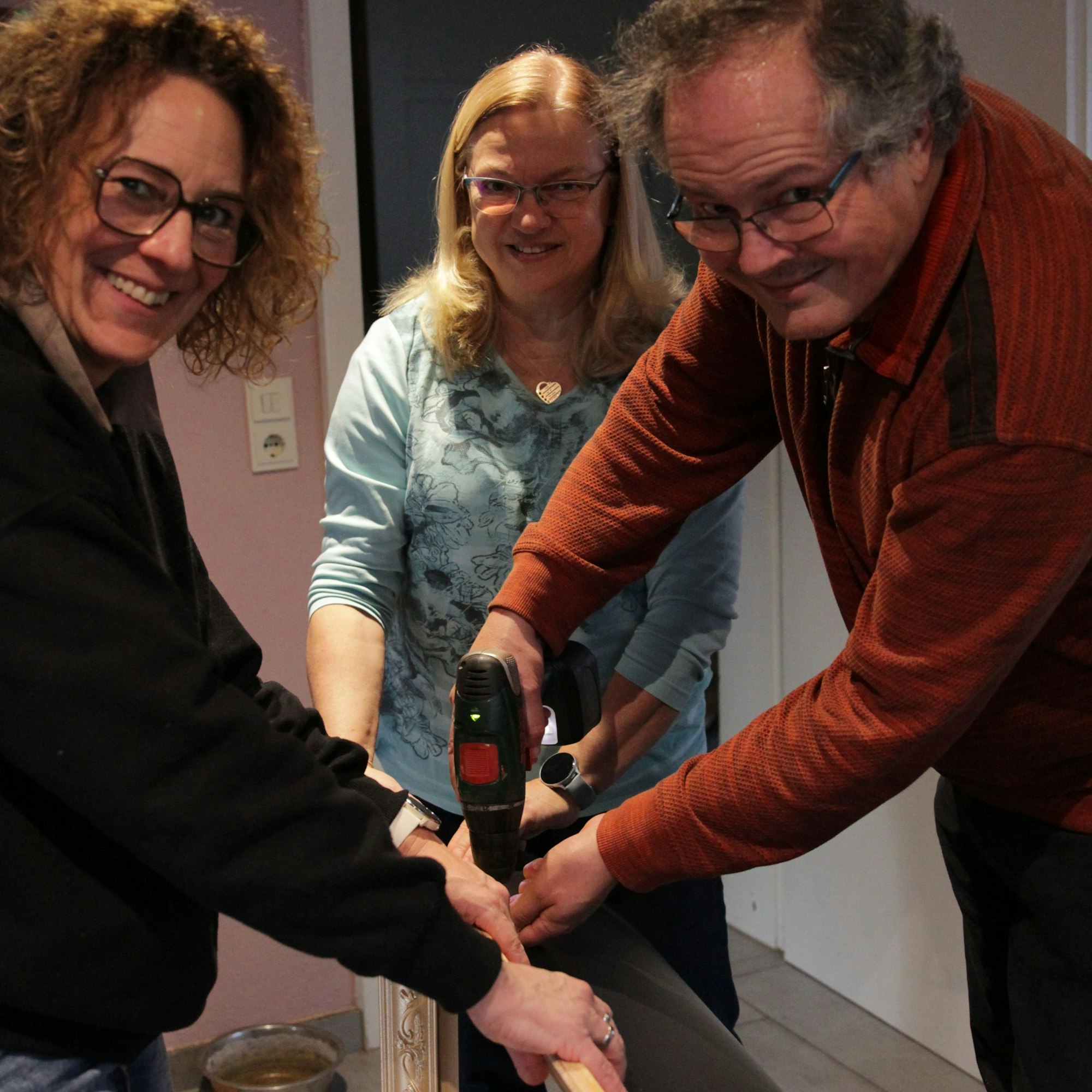 Hansgeorg Voigt schraubt zusammen mit zwei Frauen an einem Bilderrahmen.