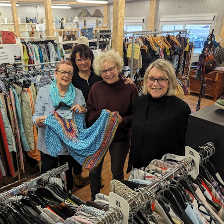 Vier Frauen zeigen ein Kleid zwischen Regalen und Kleiderständern im Gewandhaus.