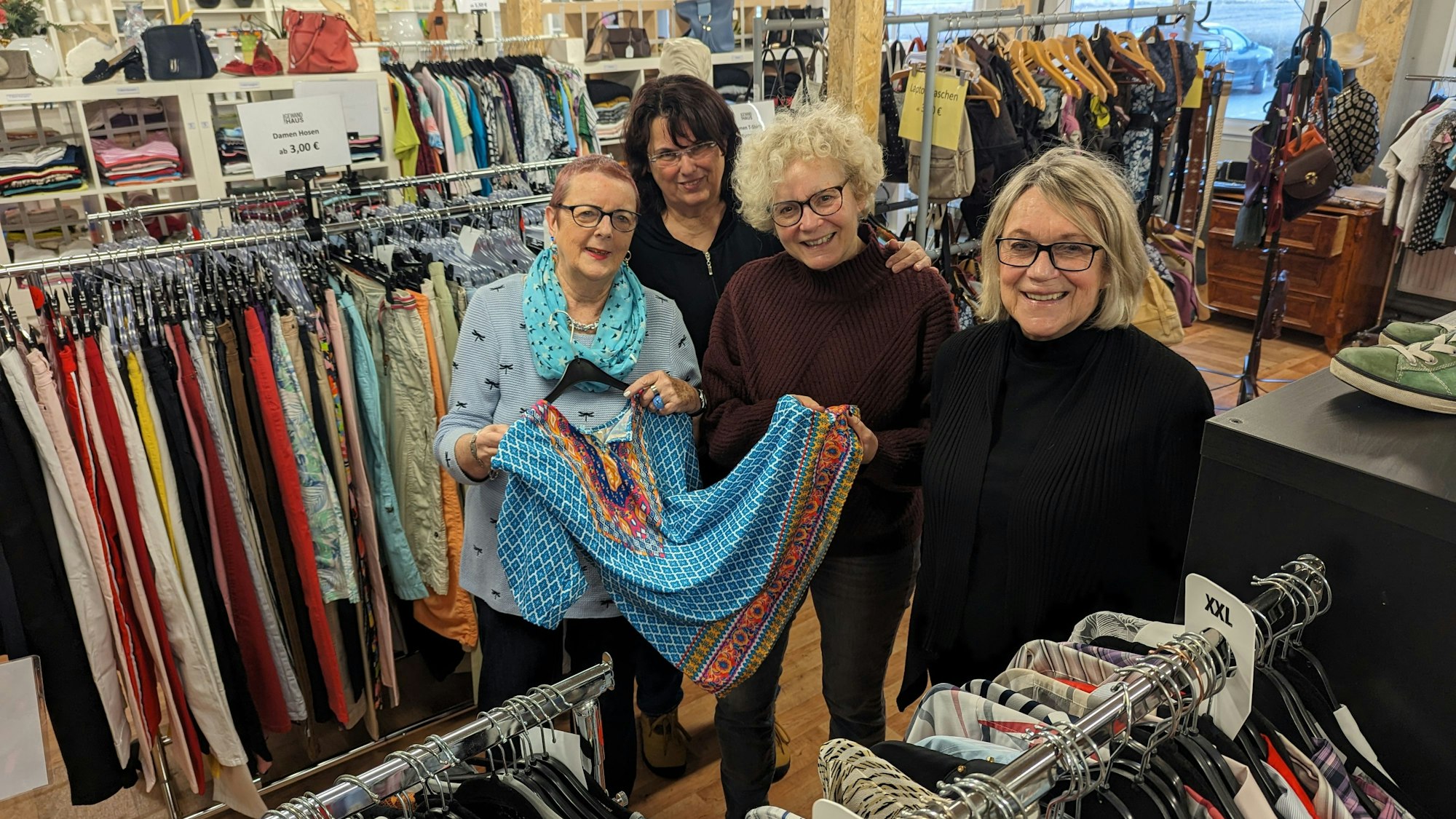Vier Frauen zeigen ein Kleid zwischen Regalen und Kleiderständern im Gewandhaus.