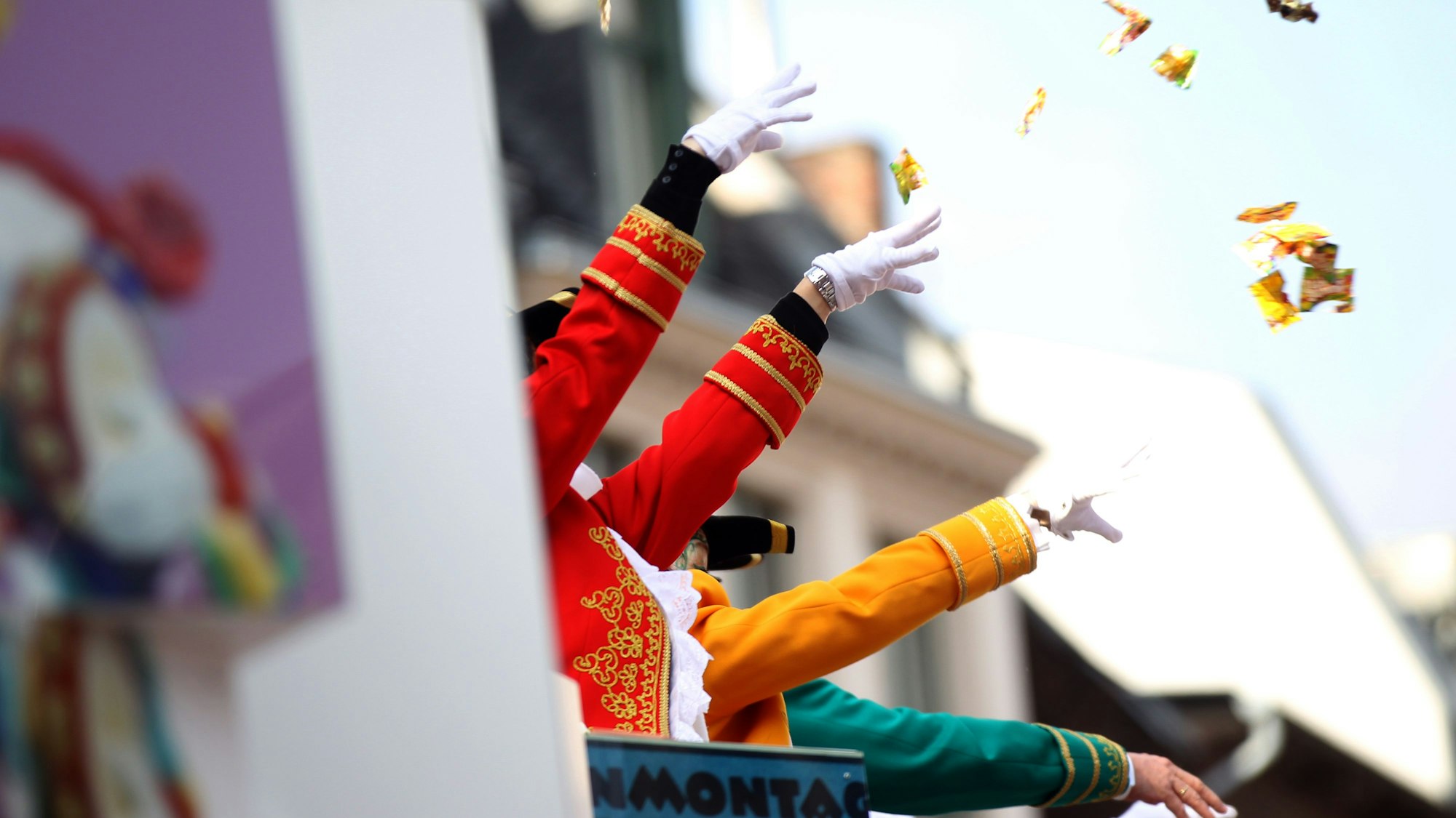 Verkleidete Jecken werfen Süßigkeiten von einem Wagen.