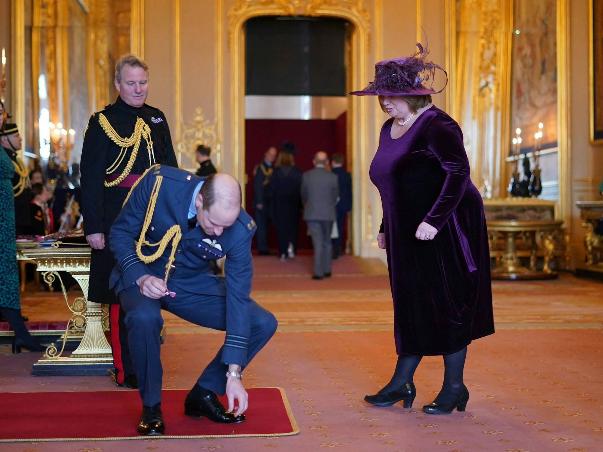 Prinz William hebt die Auszeichnung vom Boden auf, während Suzanne Hutchinson, Geschäftsführerin von Little Hearts Matter (r), auf Schloss Windsor zum Mitglied des Ordens des Britischen Empire ernannt wird.