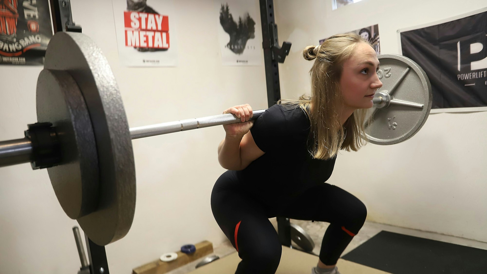 Beim Training stemmt Helena Decker Gewichte. Dabei geht sie in die Knie. Auf einem Poster im Hintergrund steht „Stay Metal“.