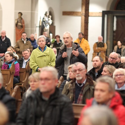In einer voll besetzen Kirche steht ein Mann und spricht in ein Mikrofon.