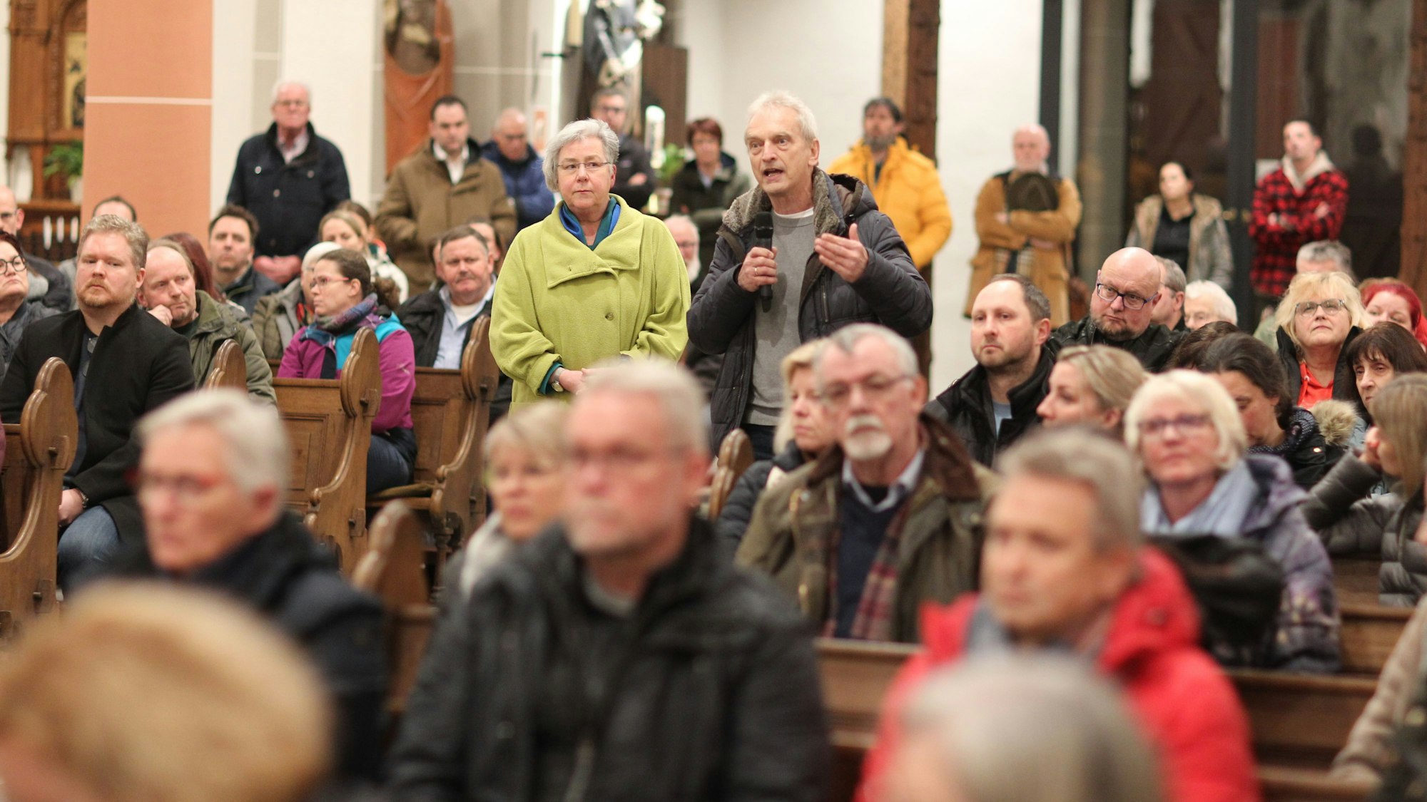 In einer voll besetzen Kirche steht ein Mann und spricht in ein Mikrofon.