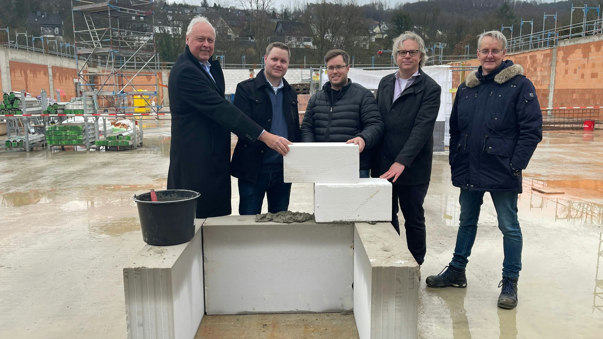 Fünf Männer stehen hinter einer Steinwand auf einer Baustelle.