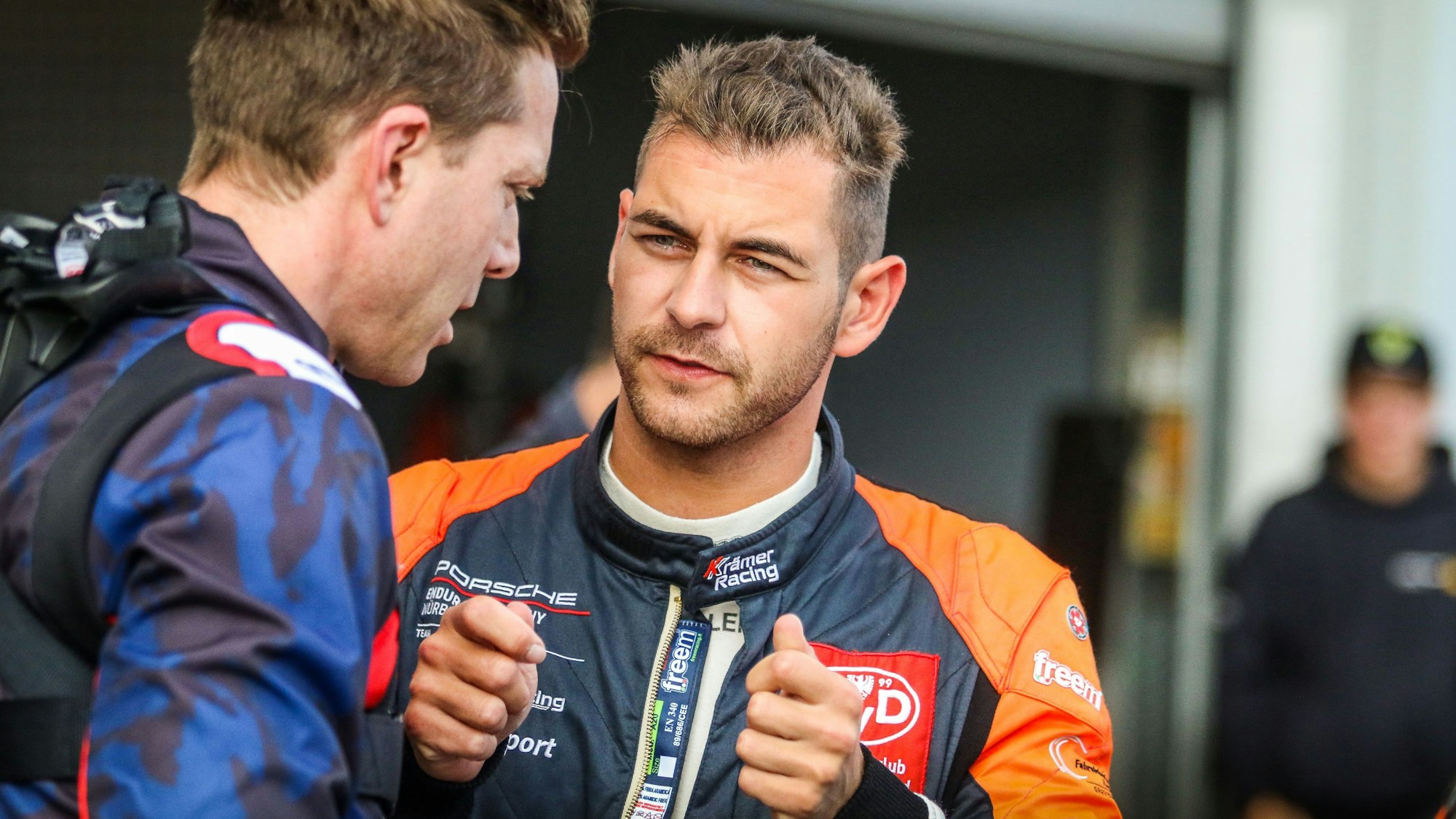 Tobias Müller im Rennoverall im Gespräch. Dabei hält er die Hände so, als ob er ein Lenkrad in den Händen hat.