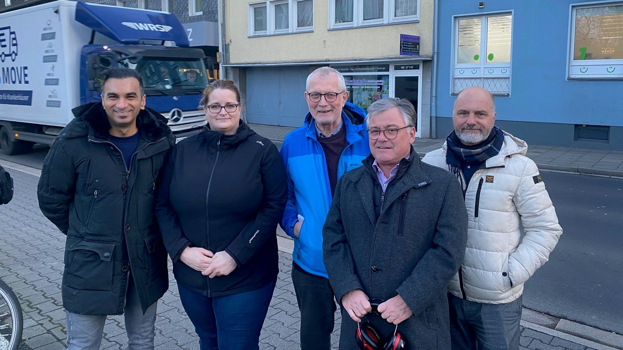 Zu sehen ist eine Gruppe von Bürgern vor der Heinrich-Esser-Straße, die gerade von einem Lkw befahren wird.