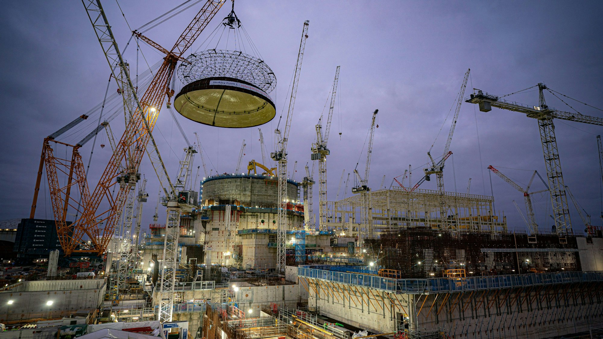 Ingenieurteams heben mit dem größten Kran der Welt - Big Carl - eine 245 Tonnen schwere Stahlkuppel auf das erste Reaktorgebäude von Hinkley Point C auf der Baustelle des Kernkraftwerks in Bridgwater, Somerset.