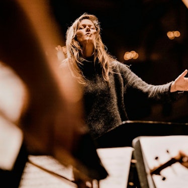 Das Bild zeigt Barbara Hannigan mit geschlossenen Augen beim Dirigieren. Im Vordergrund sind einige verschwommene Pulte mit Notenblättern zu sehen.