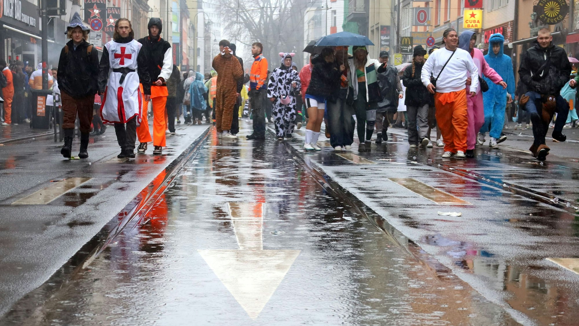 Kostümierte gehen über die nasse Zülpicher Straße.
