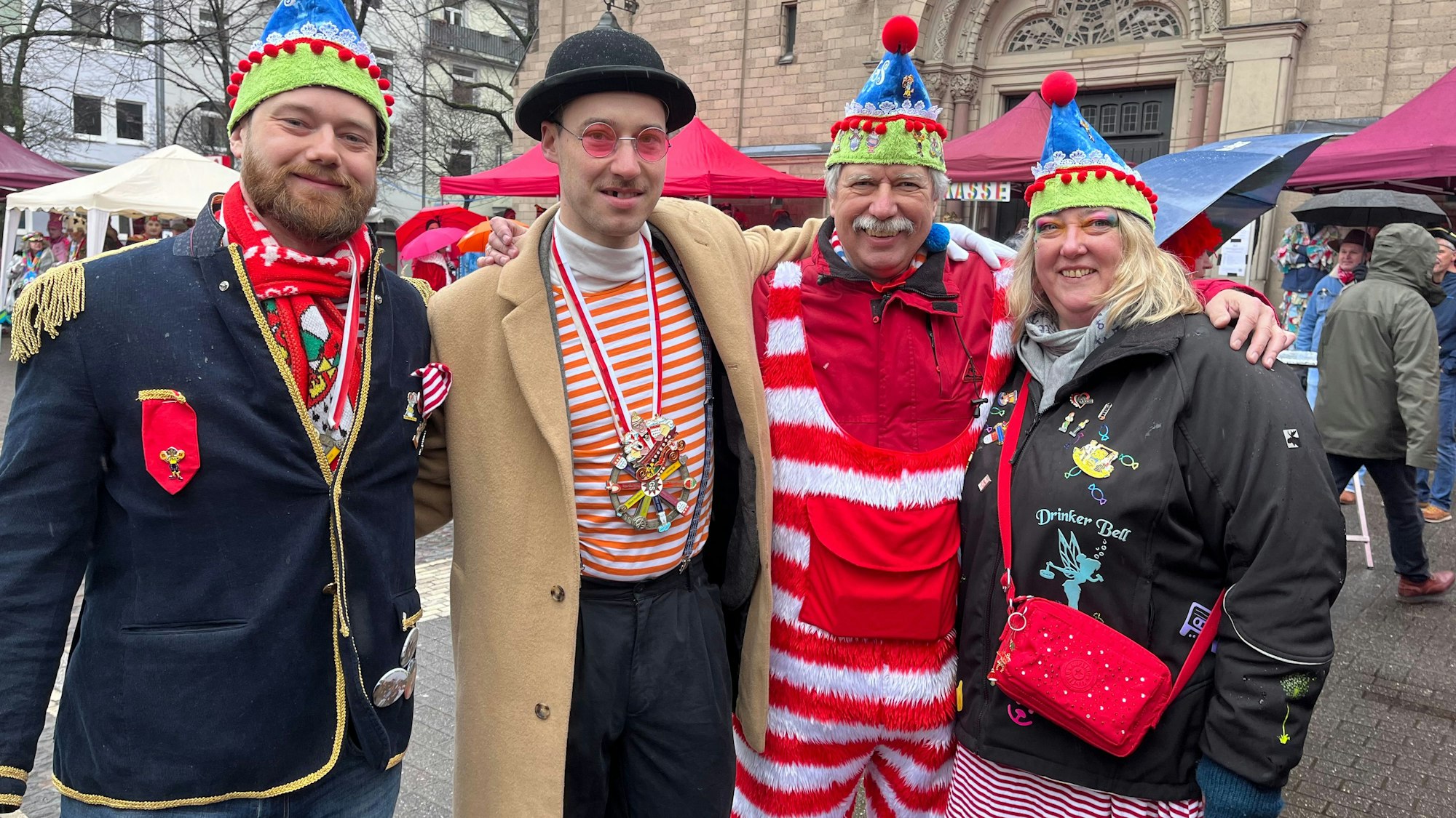 Drei kostümierte Männer und eine kostümierte Frau stehen auf einem Platz vor einer Kirche.