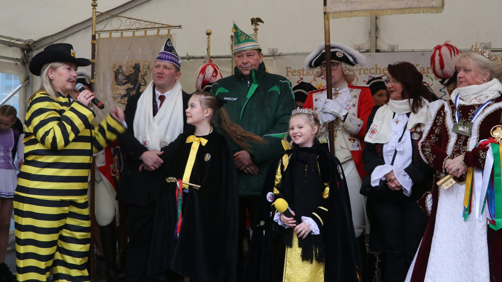 Auf dem Bild ist Frechens Bürgermeisterin und die beiden Prinzessinnen zu sehen. Hinter ihnen stehen viele karnevalistisch verkleidete Personen.