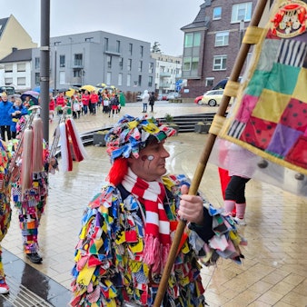 Bunt kostümierte Jecken mit Musikinstrumenten ziehen durch eine Innenstadt.