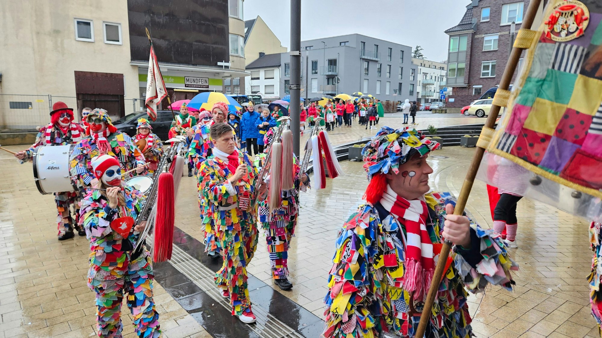 Bunt kostümierte Jecken mit Musikinstrumenten ziehen durch eine Innenstadt.