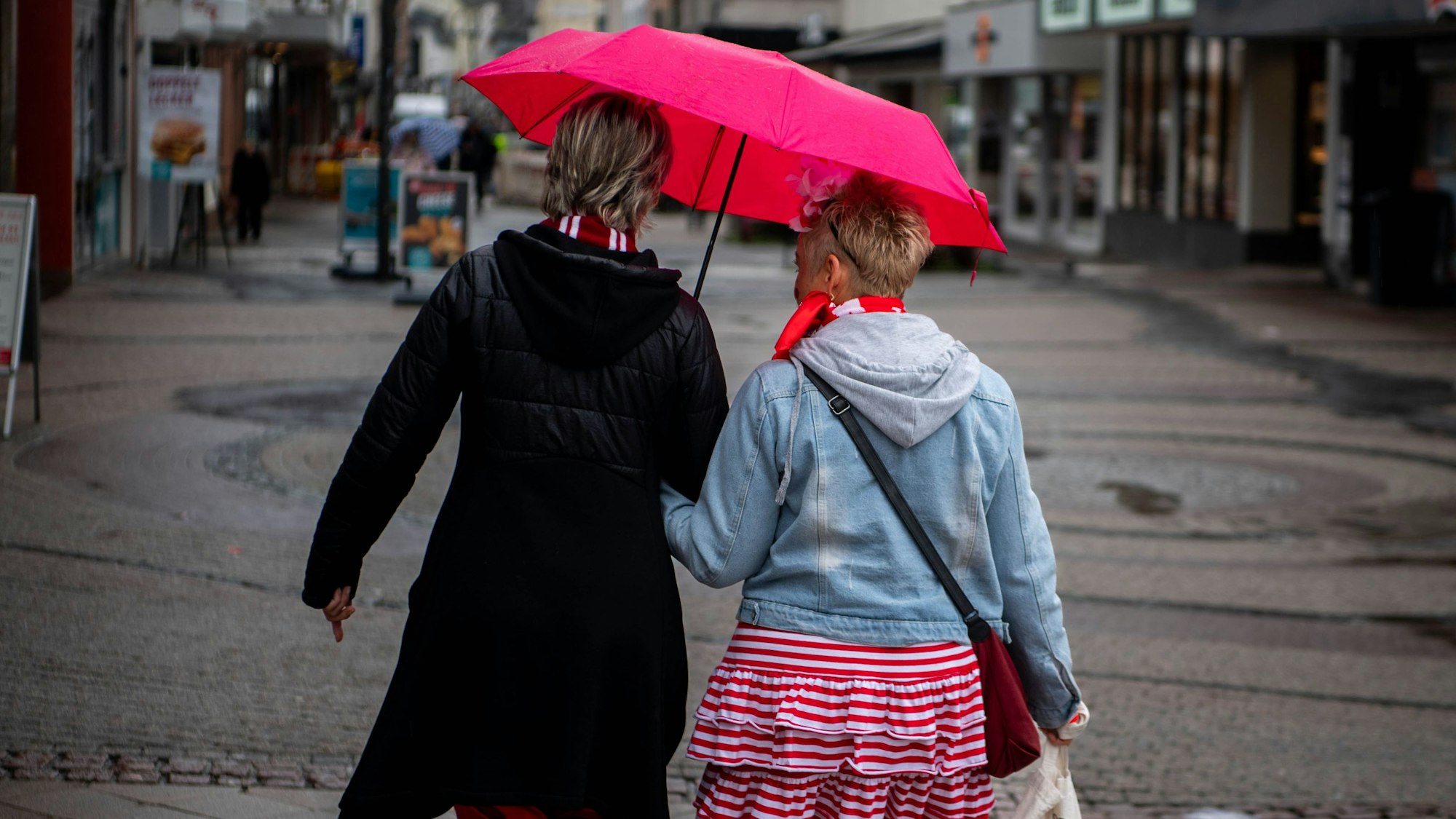Zwei Jecken gehen in der verlassen wirkenden Euskirchener Innenstadt unter einem Regenschirm.