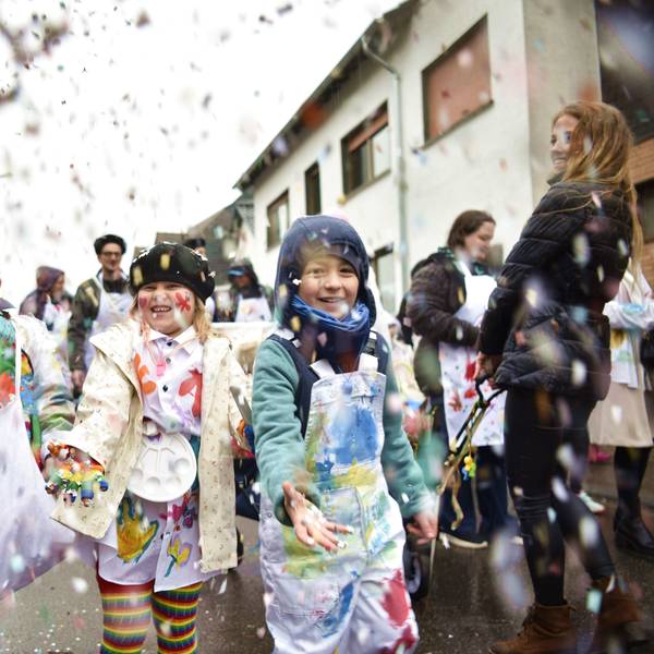 Drei zum Karneval verkleidete Kinder schmeißen beim Kinderzug in Kommern Konfetti.