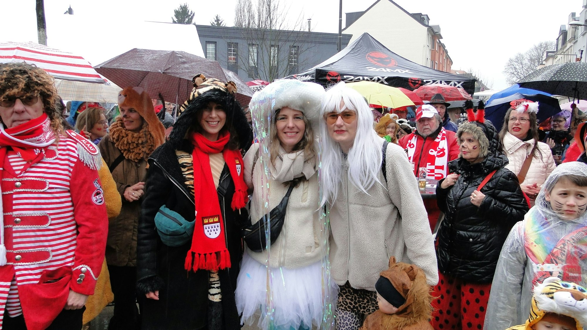 Viele verkleidete Menschen, im Vordergrund ein Frauen-Trio, stehen auf einem Platz.