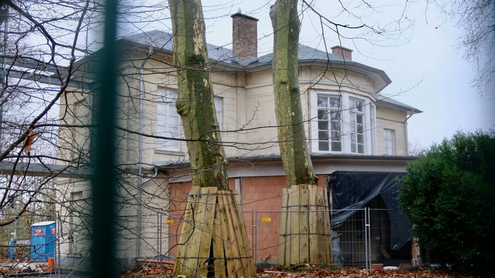 Zwei Bäume stehen vor einem abgezäunten alten Bahnhofsgebäude.