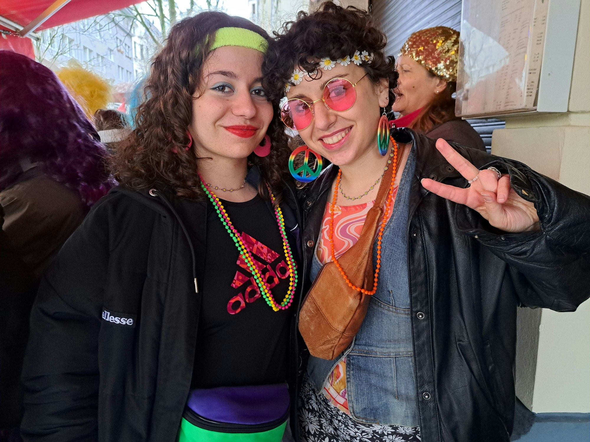Zwei junge Frauen, die als Hippies verkleidet sind, schauen in die Kamera.