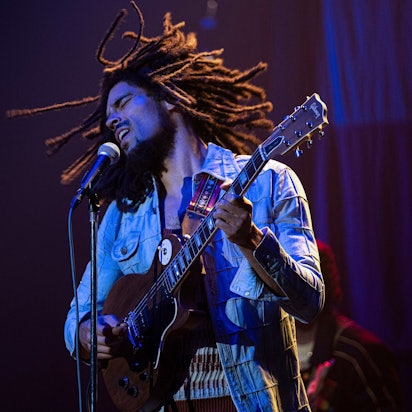 Der britische Schauspieler Kingsley Ben-Adir steht als Bob Marley Gitarre spielend und singend auf der Bühne. Er trägt eine Jeansjacke, seine Rastazöpfe