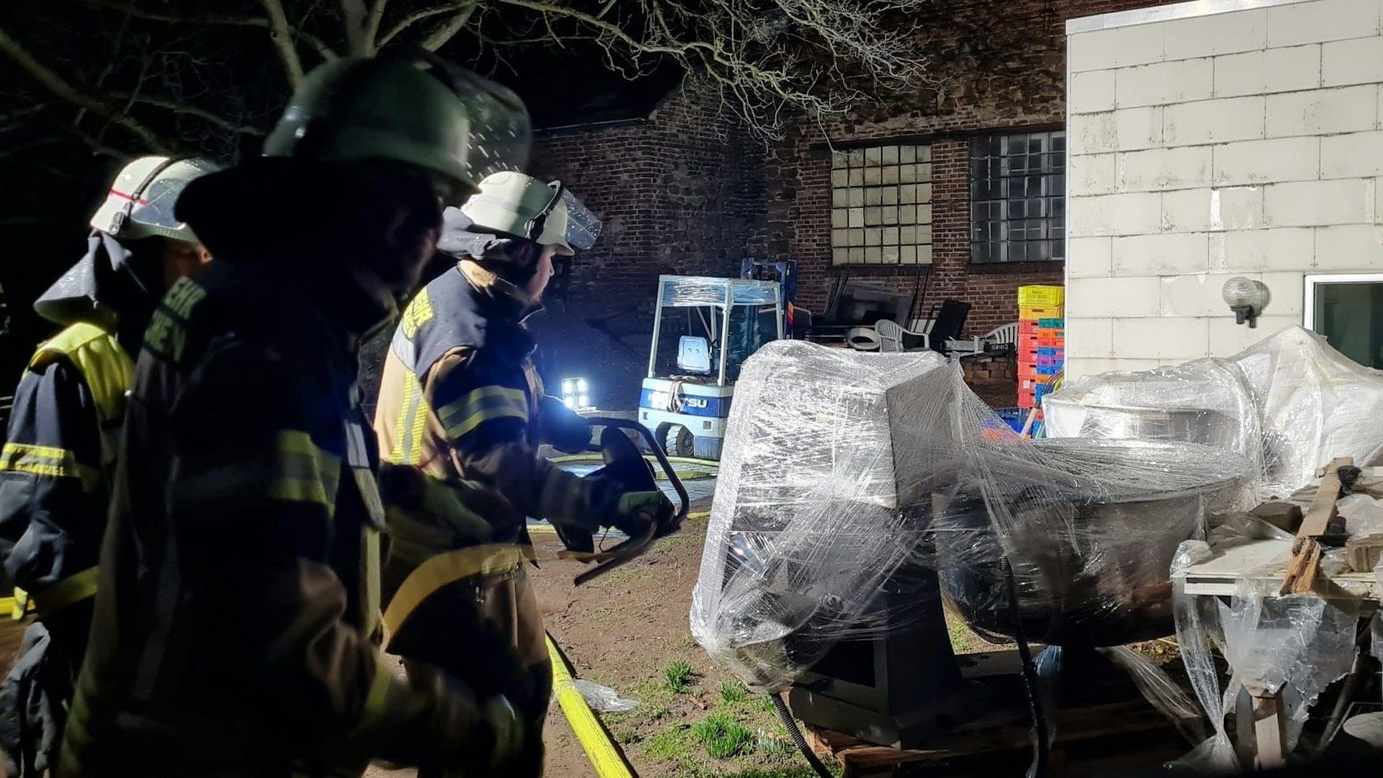 Das Bild zeigt drei Feuerwehreleute in einem Hinterhof während des Einsatzes im Bereich einer Bäckerei.