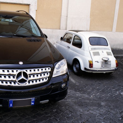 Parkende Autos: Ein großer schwarzer SUV und ein winziger weißer Fiat 500 nebeneinander eingeparkt.
